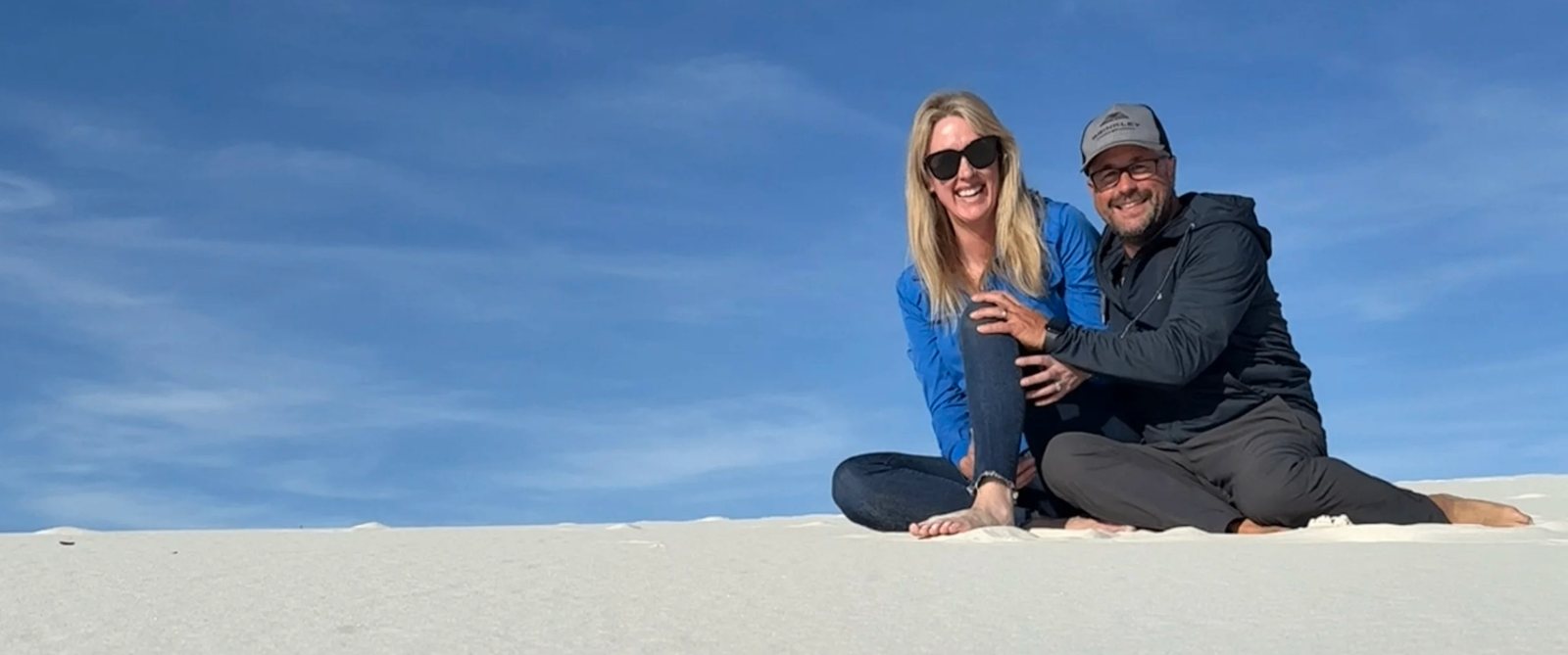 Travis and Melissa McElfresh sitting on a white gypsum dune under a blue sky at White Sands